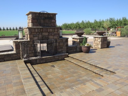 picture of a beautiful stacked stone fireplace in front of a concrete patio and stone wall in the back